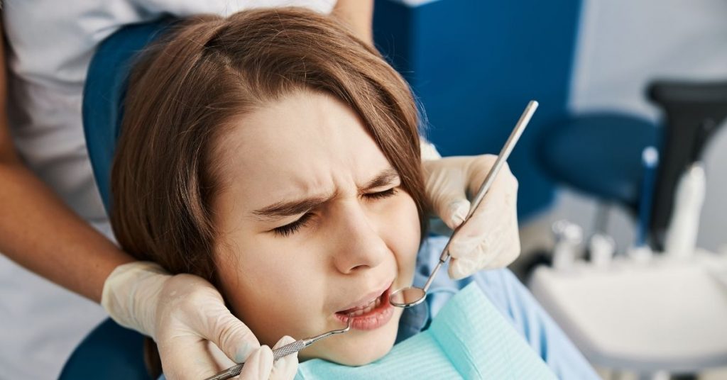 Una niña se muestra a disgusto en una sesión con el dentista en la clínica dental. 